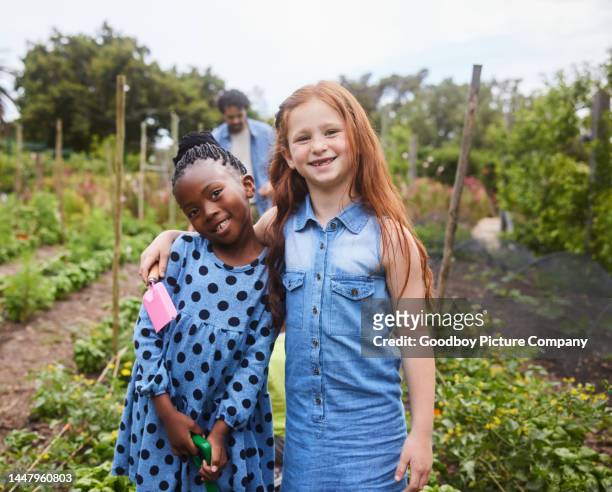 smiling young girls standing in a community garden during a class field trip - portrait of school children and female teacher in field stock pictures, royalty-free photos & images