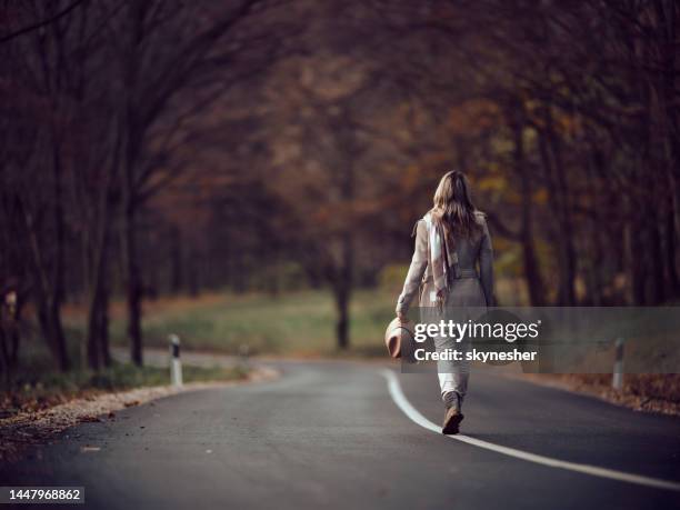 back view of a woman taking a walk on the road in autumn day. - empty road stock pictures, royalty-free photos & images