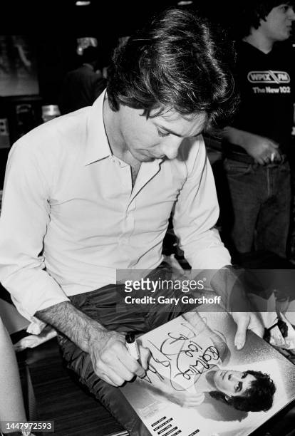 View of Australian-American Pop musician and actor Rick Springfield, seated on a desk, as he autographs an album at J&R Music store, New York, New...