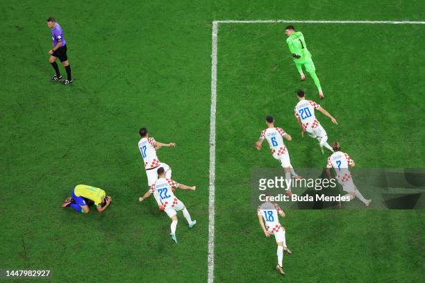 Dominik Livakovic of Croatia celebrates after Marquinhos of Brazil holds his head in dejection after his penalty hits the post for the deciding in...
