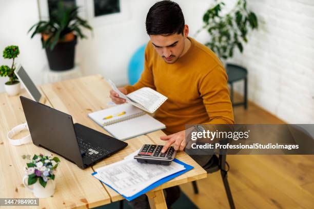 a man is working from home using a laptop and calculator to analyze business activities. - calculator stock pictures, royalty-free photos & images