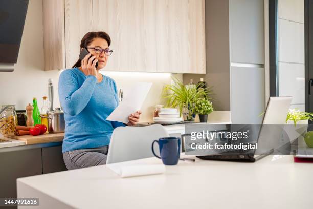 hispanic woman using phone working at home - using phone and laptop stock pictures, royalty-free photos & images