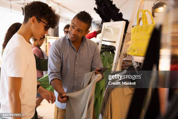 father showing t-shirt to son while shopping in store - teenager boy shopping stock-fotos und bilder