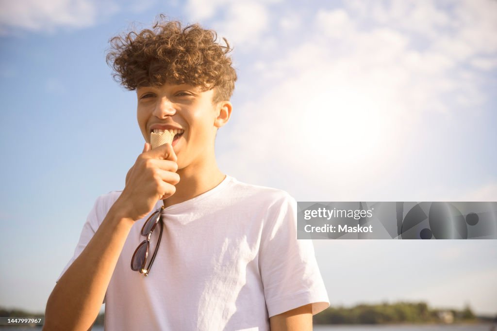 Portrait of happy teenage boy eating ice cream during vacation against sky