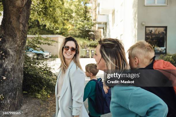 lesbian mothers talking to each other while taking sons to school - couple school stockfoto's en -beelden