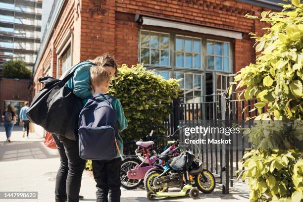 woman standing with son at school gate on sunny day - school building exterior stockfoto's en -beelden