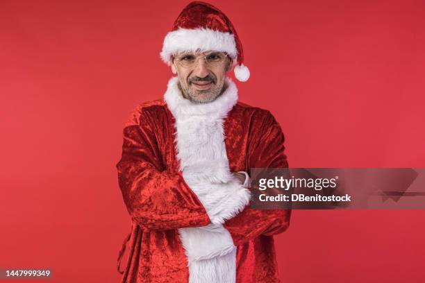 man dressed as santa claus, crossing his arms, with a serious gesture, on red background. concept of christmas, celebration, bizarre. - naughty santa 個照片及圖片檔