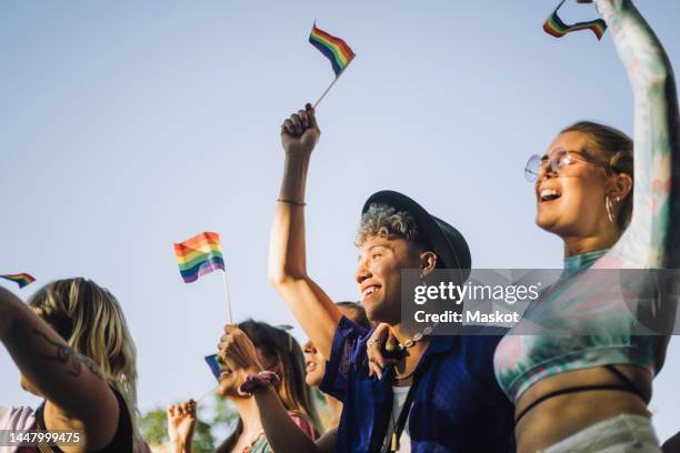 happy man and woman with hands raised holding rainbow flags while enjoying in gay pride parade - gay parade stock-fotos und bilder