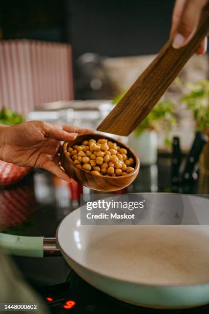 hands of female chef adding chickpea in cooking pan using wooden spoon at studio kitchen - electric stove burner ストックフォトと画像