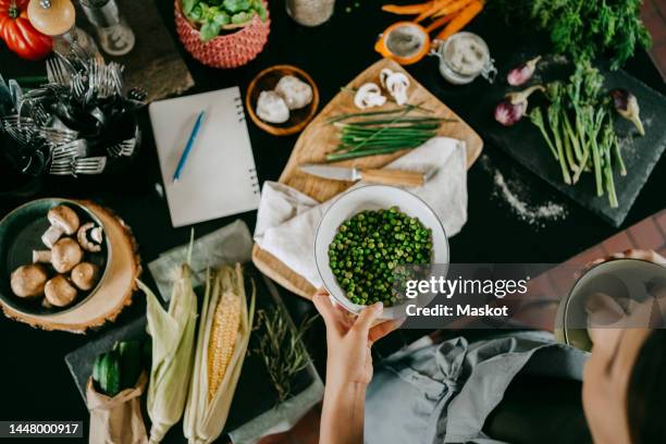 hand of female chef holding bowl of fresh green peas by counter in studio kitchen - green pea stock pictures, royalty-free photos & images