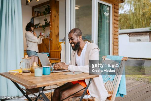 happy mature man using laptop while sitting at table on porch outside house - non moving activity bildbanksfoton och bilder