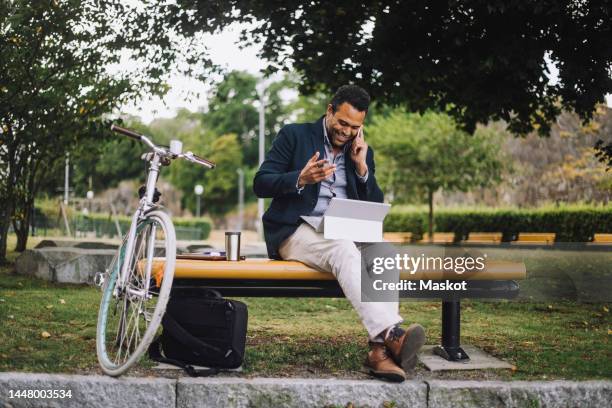 full length of male freelancer talking on smart phone while sitting in park - public park worker stock pictures, royalty-free photos & images