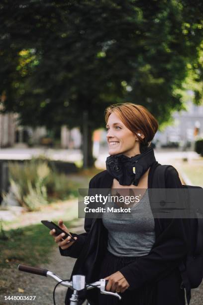 happy businesswoman with mobile phone and bicycle walking in park - krockkudde bildbanksfoton och bilder