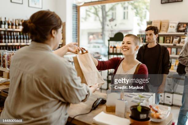 young happy female customer taking paper bag from owner at checkout counter in store - passes stock pictures, royalty-free photos & images