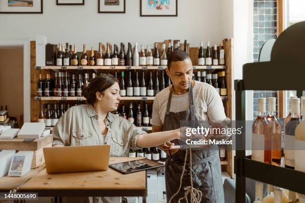 male and female owners discussing holding wine bottle at shop - liquor store stock pictures, royalty-free photos & images