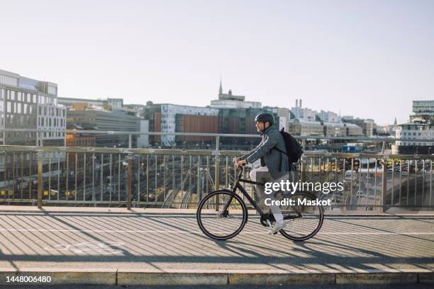 businessman riding bicycle on cycling path against buildings in city - sustainable transportation stock pictures, royalty-free photos & images