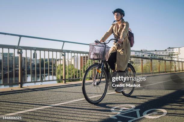 young businesswoman riding cycle on bicycle lane while commuting to work - sportschutzhelm stock-fotos und bilder