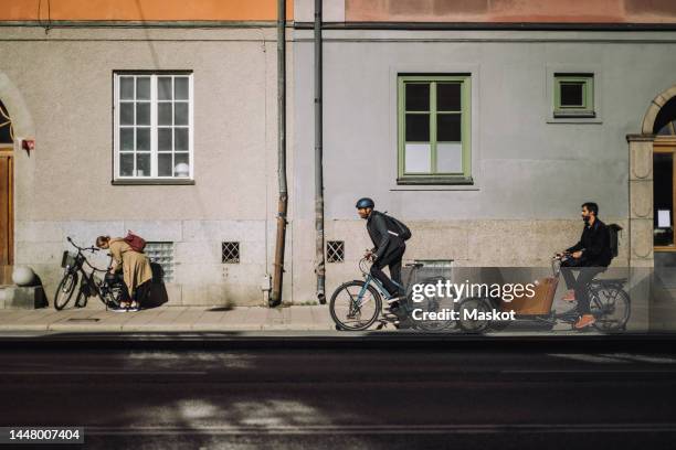 male commuters riding bikes on road against building during sunny day - sustainable transportation stock pictures, royalty-free photos & images