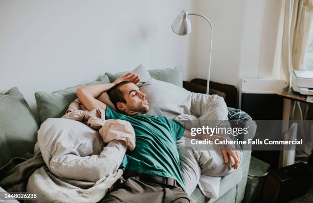 a man is asleep on a sofa surrounded by duvets and pillows - schnarchen mann stock-fotos und bilder