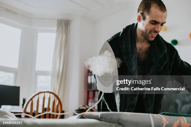 a man wearing a dressing gown irons a green t-shirt - bügelbrett stock-fotos und bilder