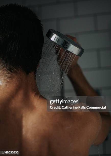 a man holds a shower head over his shoulder - queimadura pele - fotografias e filmes do acervo