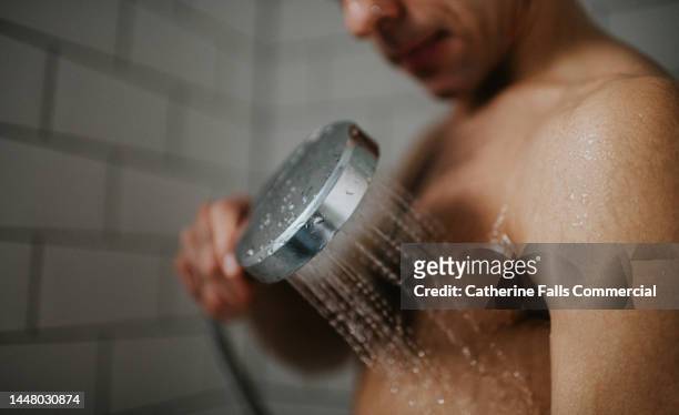 a man washes his chest with a shower head - olor desagradable fotografías e imágenes de stock