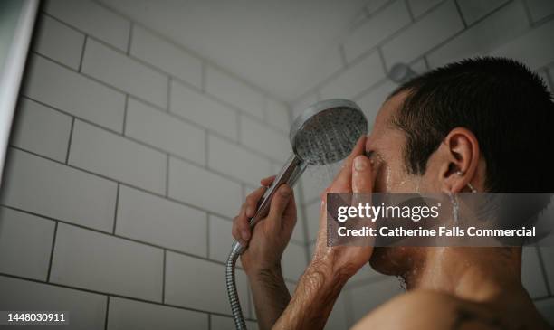 a man showers in a white, tiled bathroom, focusing on his face. - shower stock pictures, royalty-free photos & images