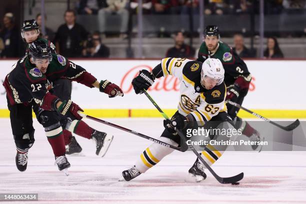 Brad Marchand of the Boston Bruins skates with the puck ahead of Jack McBain of the Arizona Coyotes during the second period of the NHL game at...
