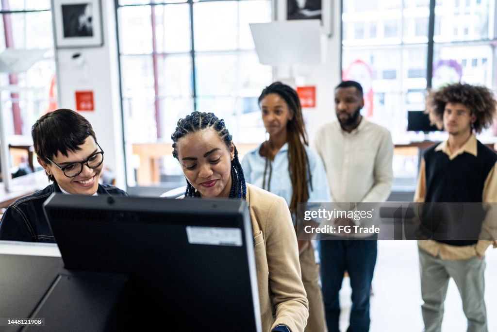 Friends using the self checkout to borrow book from the library - including a transgender person
