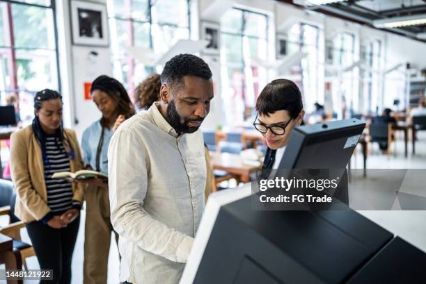 friends using the self checkout to borrow book from the library - including a transgender person - self checkout line stock pictures, royalty-free photos & images
