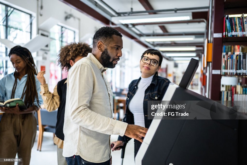 Friends using the self checkout to borrow book from the library - including a transgender person