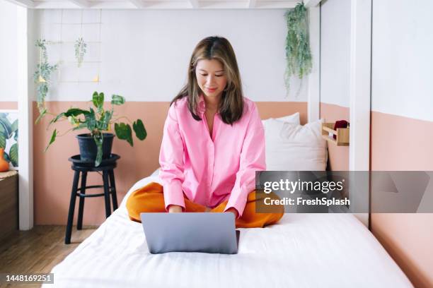 uma bela empresária feliz em camisa rosa e calças laranjas trabalhando em casa usando seu computador - calças verdes - fotografias e filmes do acervo