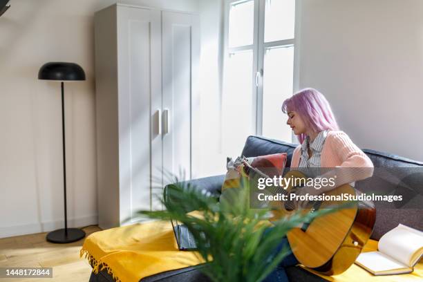 a young female musician is practicing playing an acoustic guitar at home. - international artists stock pictures, royalty-free photos & images