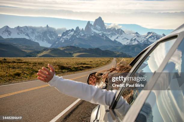 woman chilling and holding her hand outside of window while on the  highway to the dramatic mountain range with fitz roy mountain in the middle - a road to el chalten from el calafate, argentina - patagonia chile - fotografias e filmes do acervo