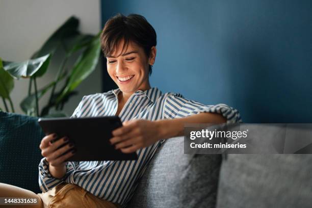 portrait of a happy woman resting on the sofa and using a digital tablet - watching ipad stock pictures, royalty-free photos & images