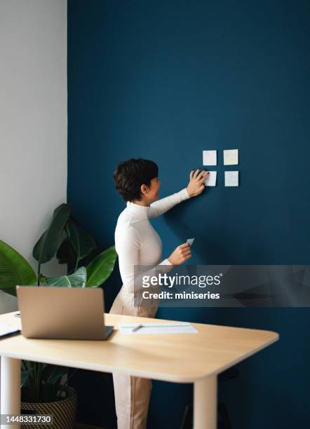 unrecognizable businesswoman putting post it notes on the wall and organizing work - blue note pad stock pictures, royalty-free photos & images