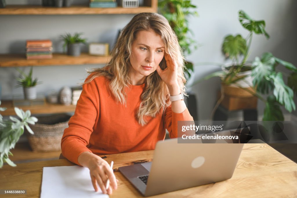 Mature adult woman working at home (laptop, document, negative emotions)