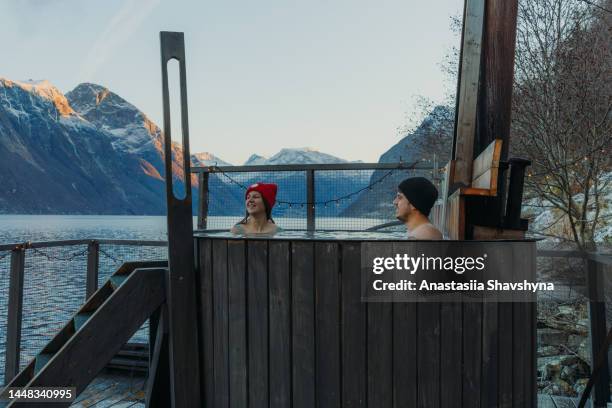 a woman and a man relaxing in hot tub with scenic mountain view by the fjord in winter in norway - sauna winter stockfoto's en -beelden