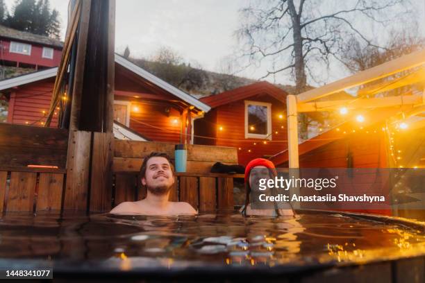 donna e uomo felici che si rilassano nella vasca idromassaggio con vista panoramica sulle montagne dal fiordo in inverno in norvegia - sauna winter foto e immagini stock