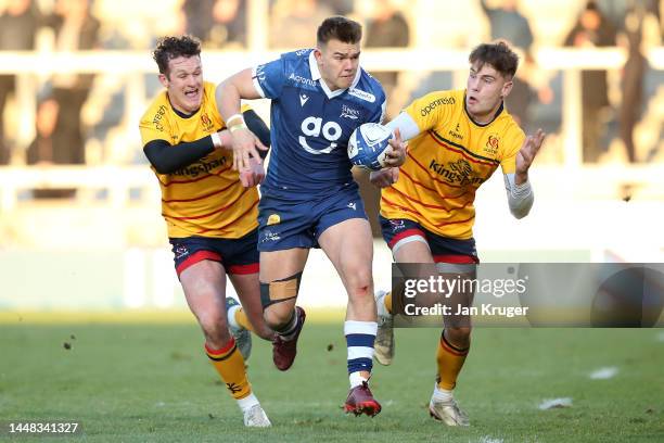 Joe Carpenter of Sale Sharks breaks through the defence of Ethan McIlroy and Billy Burns of Ulster during the Heineken Champions Cup match between...