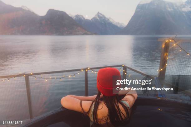 rear view of a woman in red hat relaxing in hot tub with scenic view of the winter fjord in norway - röd hatt bildbanksfoton och bilder