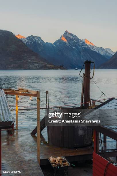 vista posteriore di un uomo che si rilassa nella vasca idromassaggio con vista panoramica del fiordo invernale in norvegia - sauna winter foto e immagini stock