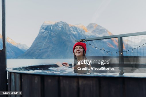 Side view of a happy woman in red hat relaxing in hot tub with scenic view of the winter fjord in Norway Side view of a happy woman in red hat relaxing in hot tub with scenic view of the winter fjord in Norway