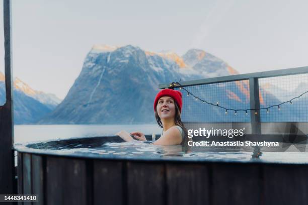 side view of a happy woman in red hat relaxing in hot tub with scenic view of the winter fjord in norway - red tub 個照片及圖片檔