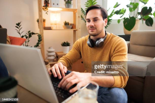 young casually clothed man working from the comfort of his living room - quarantine stock pictures, royalty-free photos & images