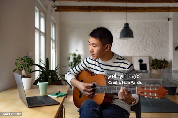asian man having an online guitar lesson at home. - muzieksymbool stockfoto's en -beelden