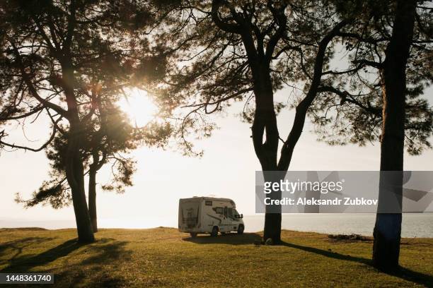 a white trailer, a van, parked on a hill in the middle of the forest. mobile home on the seashore, beach. summer holidays with family, camper for travel, ecotourism, recreation, autonomous camping, road trip, van. beauty in nature, picturesque landscape. - rv beach foto e immagini stock