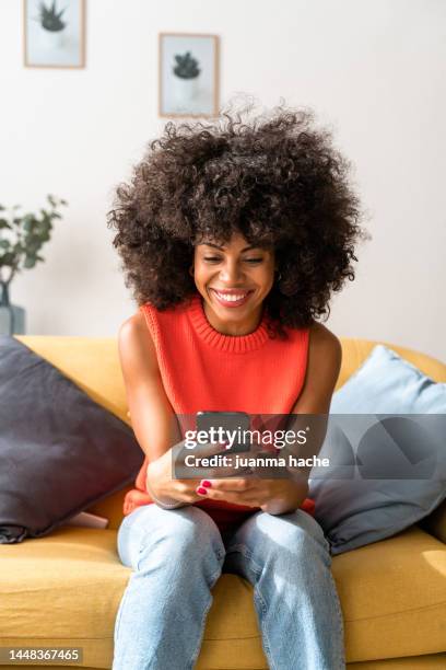 smiling woman sitting in living room while texting with mobile phone to her friends to have lunch together. . - person looking at phone fotografías e imágenes de stock