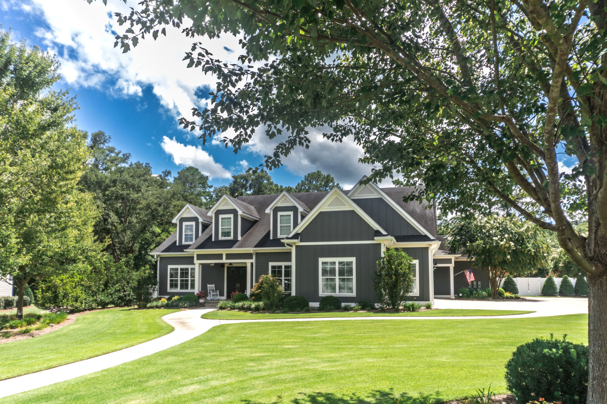 A large gray craftsman new construction house with a landscaped yard and leading pathway sidewalk A large gray craftsman new construction house with a landscaped yard and leading pathway sidewalk