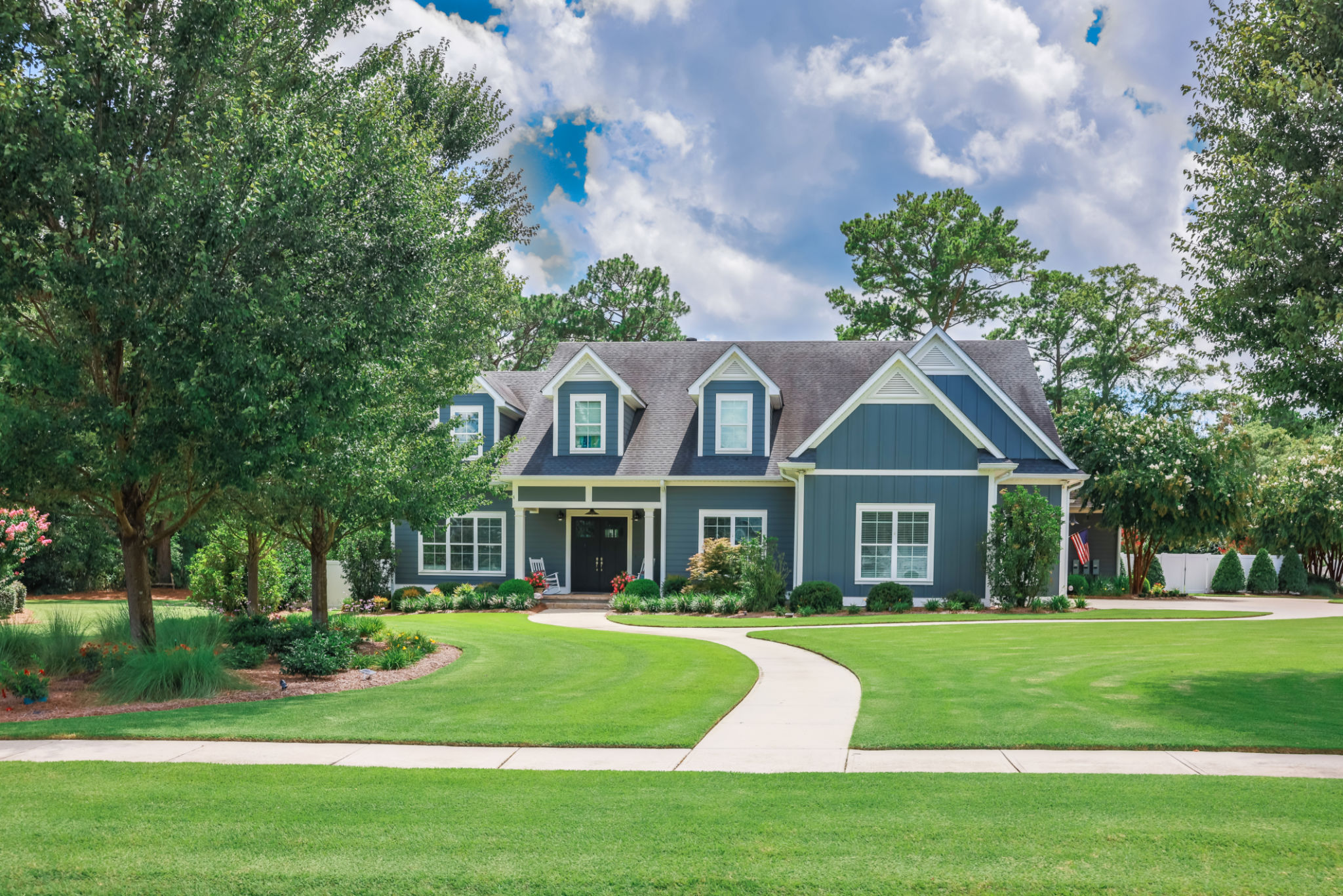 A large blue craftsman new construction house with a landscaped yard and leading pathway sidewalk A large blue craftsman new construction house with a landscaped yard and leading pathway sidewalk